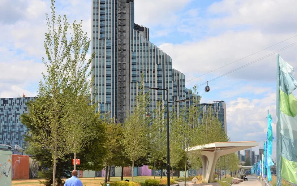 A man walking along a sidewalk beside a tall building, with a clear blue sky in the background.